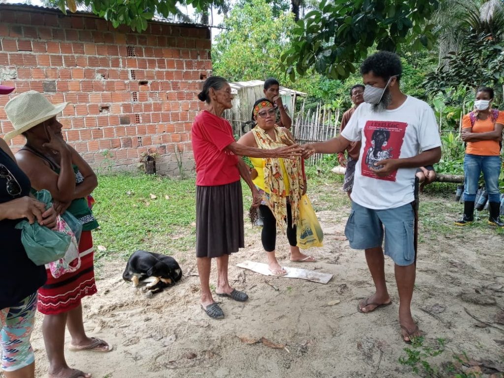Mestre Joelson, co-fundador da Teia dos Povos, entrega sementes para uma das mais velhas da Aldeia Tukun do povo Tupinambá, Mestra Nádia e outros tupinambá olham atentamente o gesto.